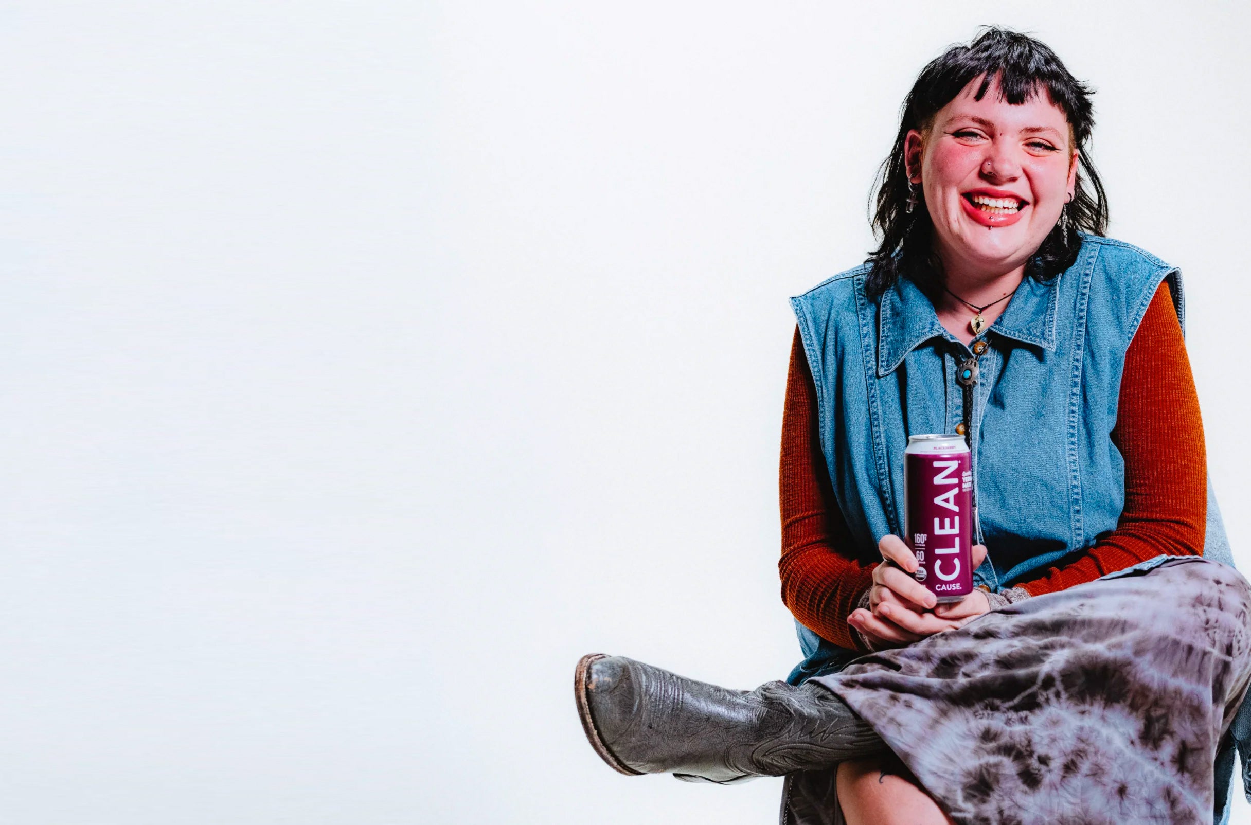 Person sitting in front of a white background smiling while holding a can of Blackberry CLEAN.