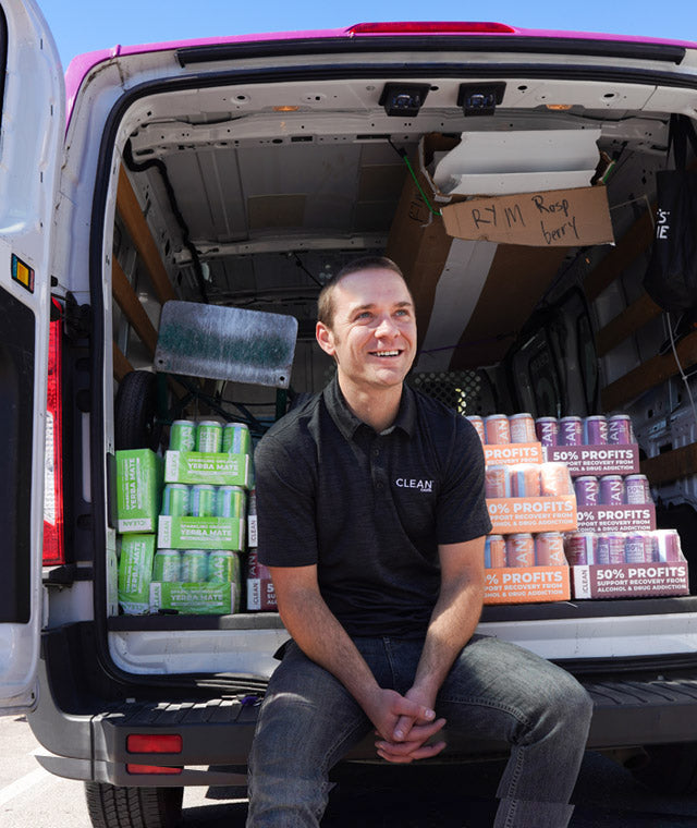 Man sitting in the back of an open van with cases of Lemon Lime, Peach, and Blackberry CLEAN in the back.