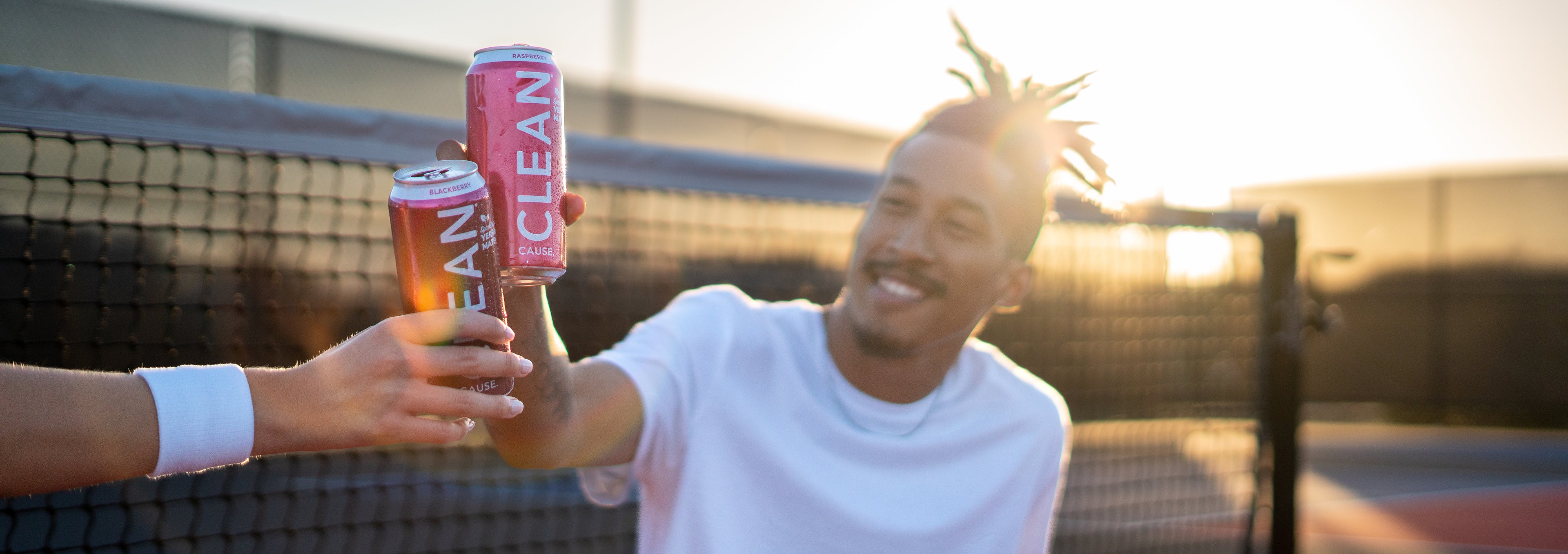 Man on court cheersing with a person out of frame. They're holding a Raspberry and Blackberry CLEAN respectively.